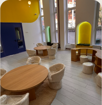 Warm TALENTA.KIDS learning room with round tables, soft seating, and natural light